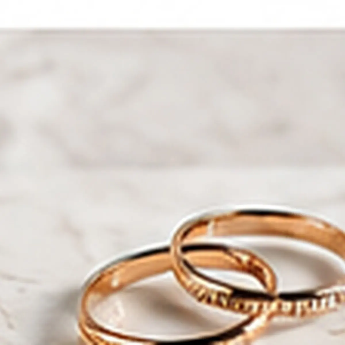 Gold rings on a pale marble surface in a clean premium jewelry product scene